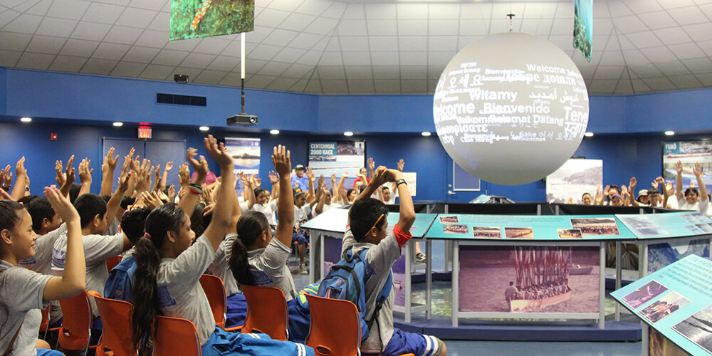 Students raise their hands while facing sphere with words projected on it